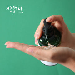 Hand holding a bottle LikeDew 90% Aloe Vera Gel being poured onto another hand against a green background