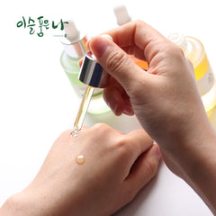 Hand holding a dropper with a yellow liquid over another hand on a white background, with a brand name in the corner.