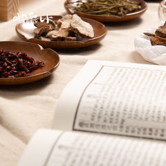 Herbal ingredients on wooden plates with an open book on a textured surface