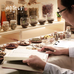 Person studying herbs with various containers and books on a table