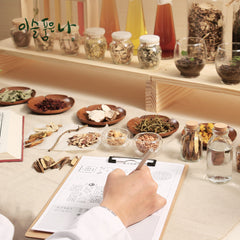 Person taking notes with herbs and bottles on a table, possibly in an educational setting.