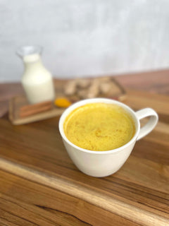 White mug with yellow liquid on a wooden surface, with a blurred background