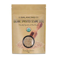 Paper package of organic sprouted sesame seeds with a wooden scoop on a white background.